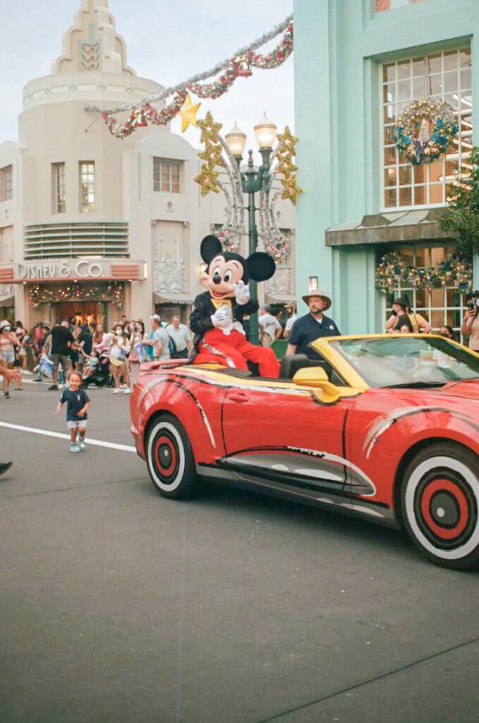 Mickey Mouse sitting in a red convertible in a parade going down the main street of Hollywood Studios at Walt Disney World in Orlando Florida